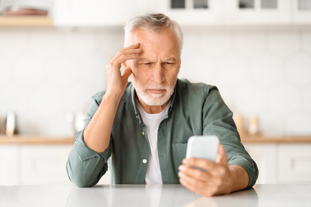 Senior man squinting and rubbing forehead while reading phone